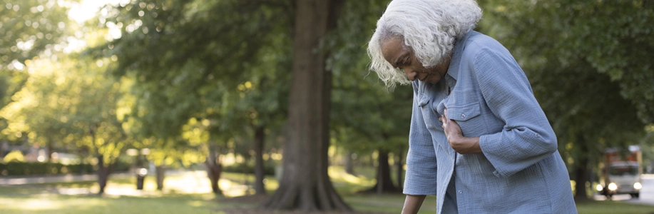 Older woman outside bends over with hand on chest