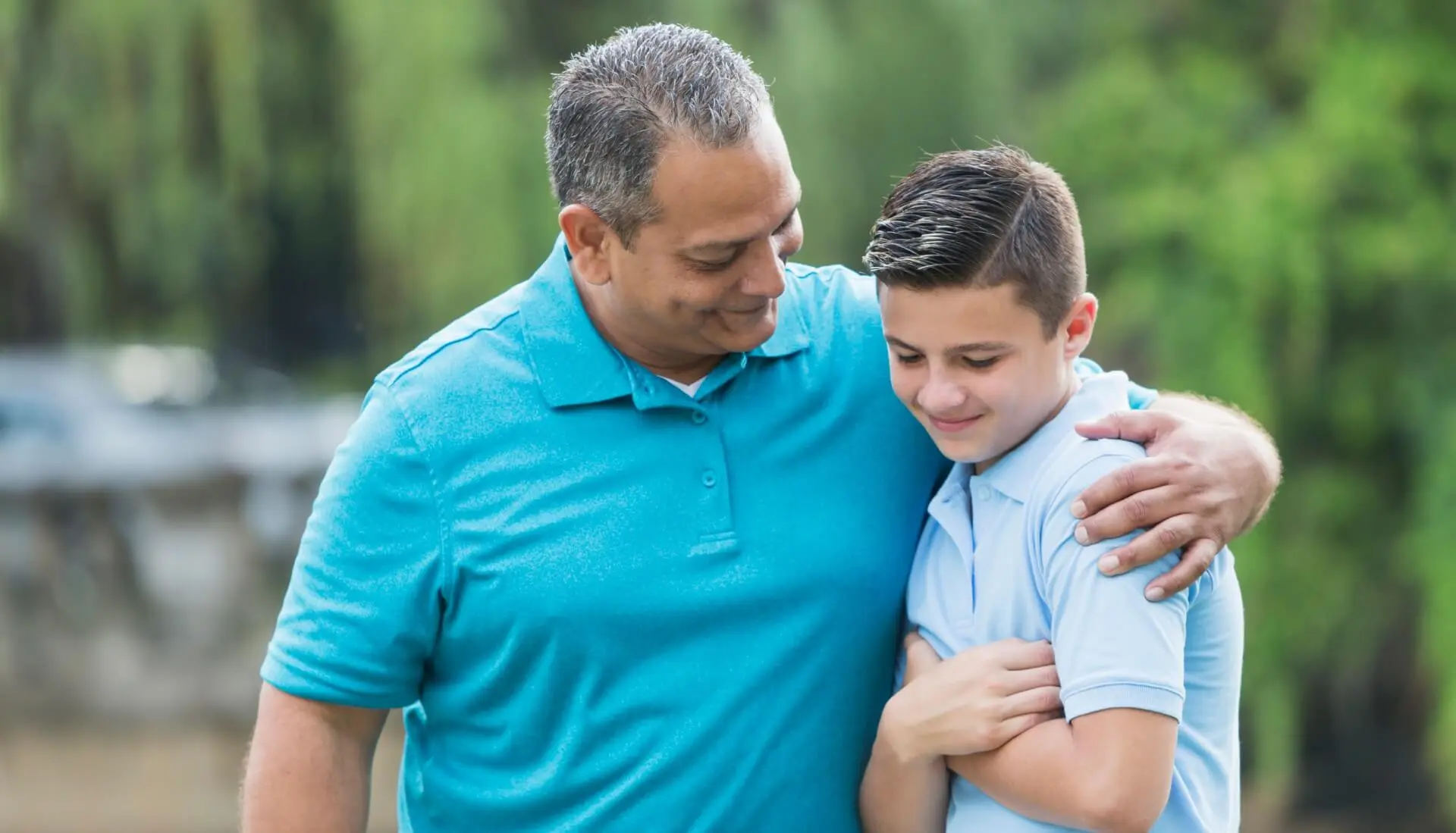 Father in blue shirt puts his arm around teenage son in lighter blue shirt