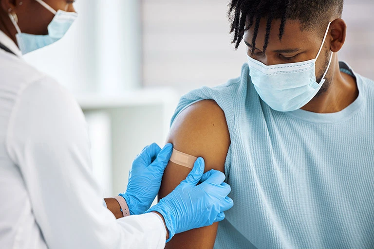 Doctor wearing a mask puts band-air on patient wearing a mask's arm.