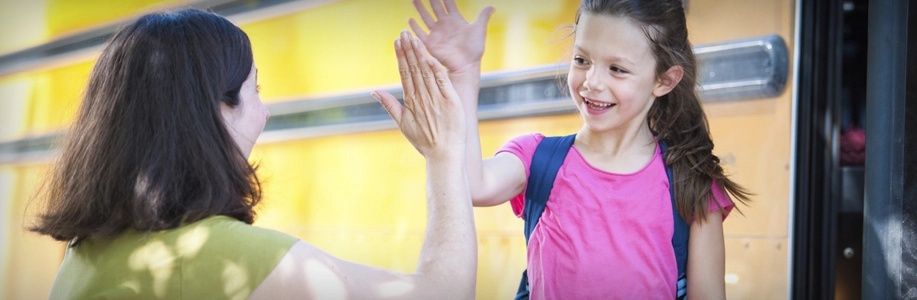 Young student high fives her mom in front of school bus