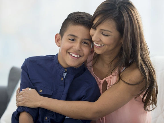 Mother in pink tank top hugs teen son who wears a navy shirt