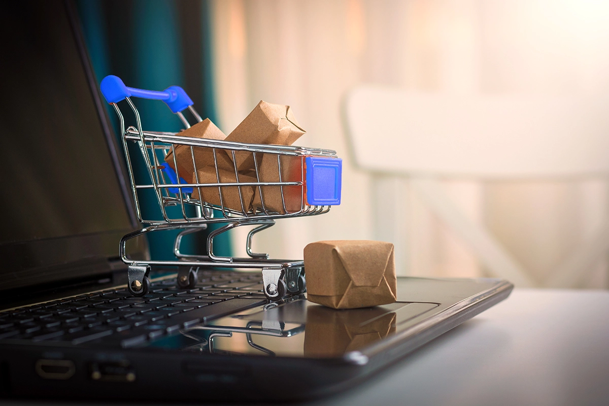 Miniature shopping cart with packages sitting on top of a laptop